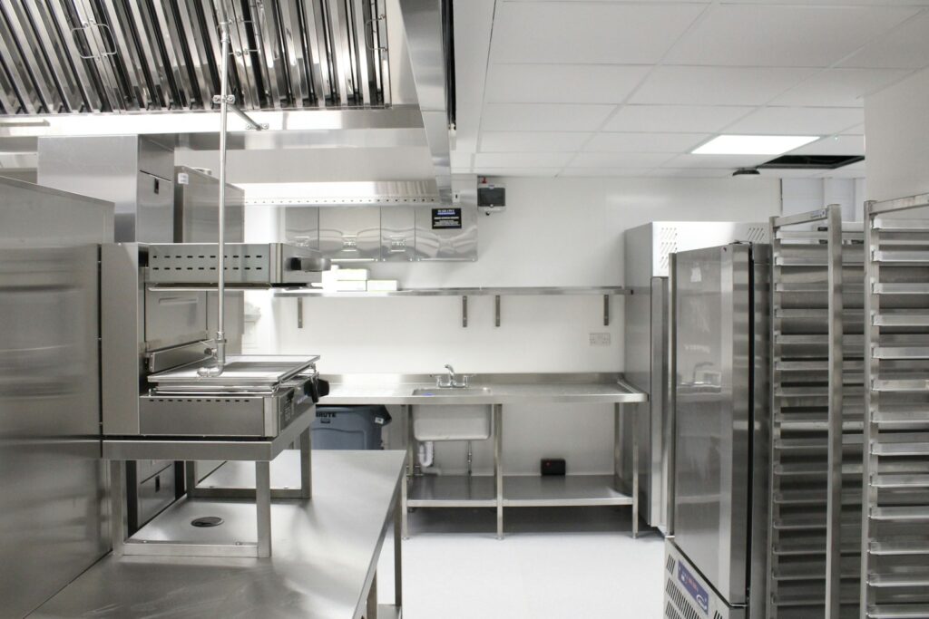 Back-of-house commercial kitchen with stainless steel refrigeration, extraction canopy and storage racking, as prepared during installation