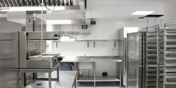 Back-of-house commercial kitchen with stainless steel refrigeration, extraction canopy and storage racking, as prepared during installation