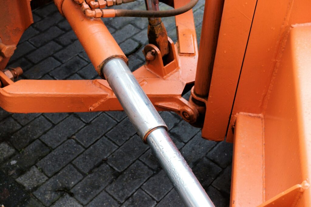 Hydraulic cylinder attached to orange machinery, the kind of component protected by hard chrome plating