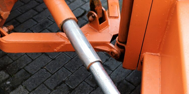 Hydraulic cylinder attached to orange machinery, the kind of component protected by hard chrome plating