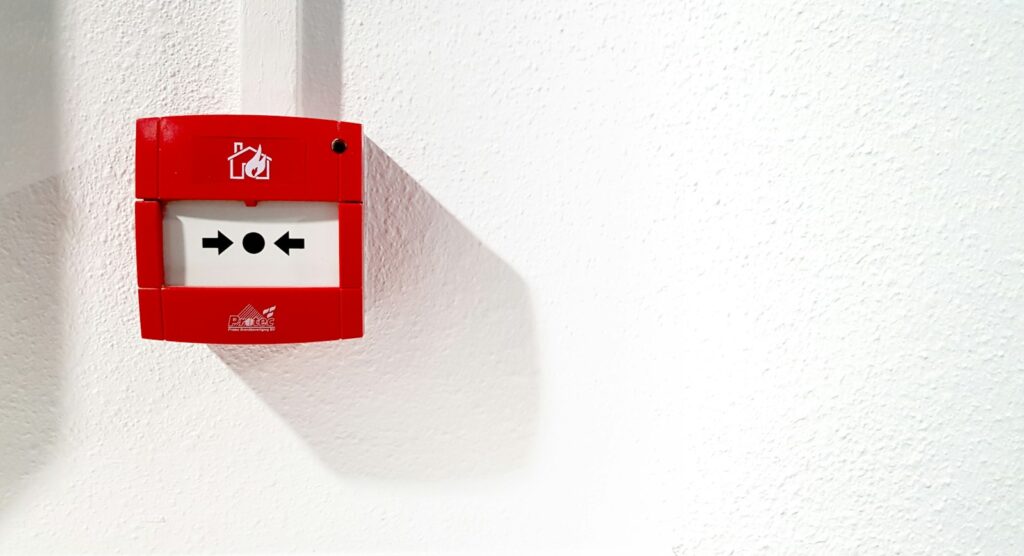 Fire alarm with a break glass cover mounted on a white wall for emergency use