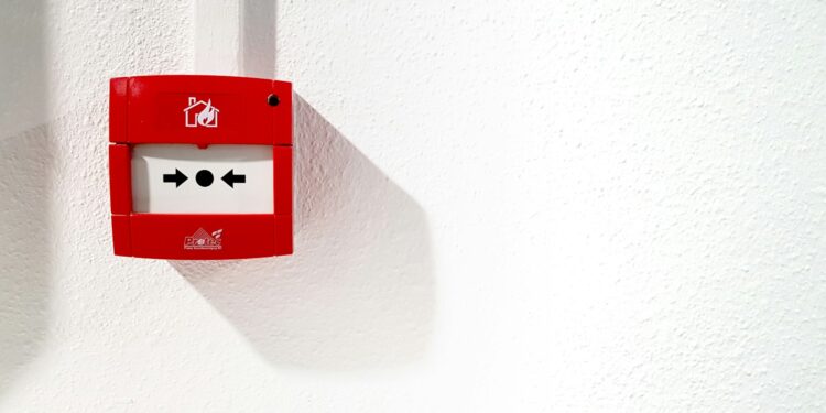 Fire alarm with a break glass cover mounted on a white wall for emergency use