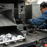 A man working at a machine in a factory, illustrating production scheduling for surface-treated metal parts