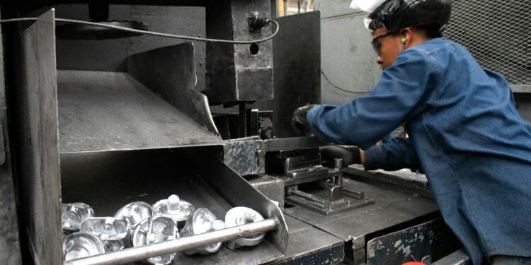 A man working at a machine in a factory, illustrating production scheduling for surface-treated metal parts