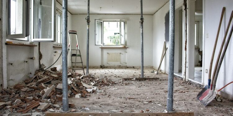 A room under renovation with metal support poles, debris and tools on the floor
